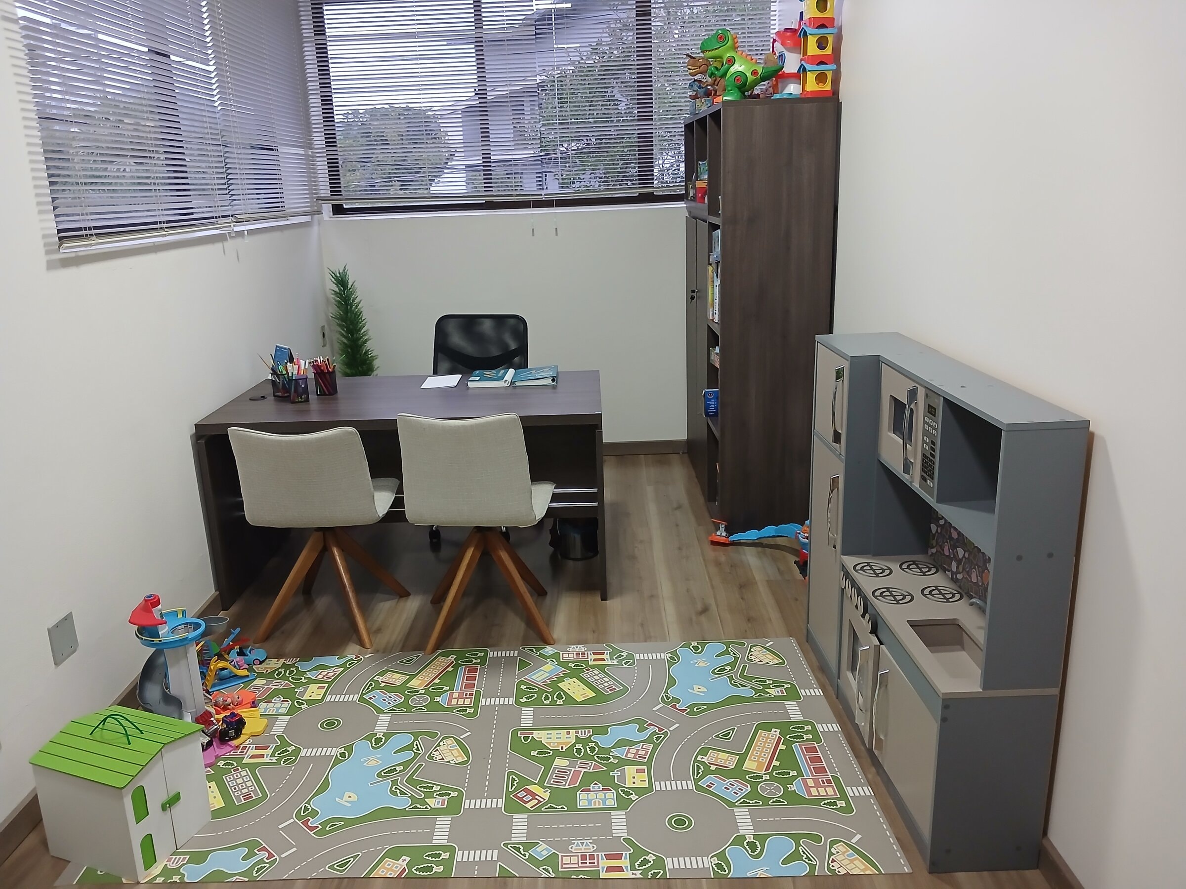 Consultório de Parobé com mesa de atendimento, brinquedoteca e estante de materiais lúdicos